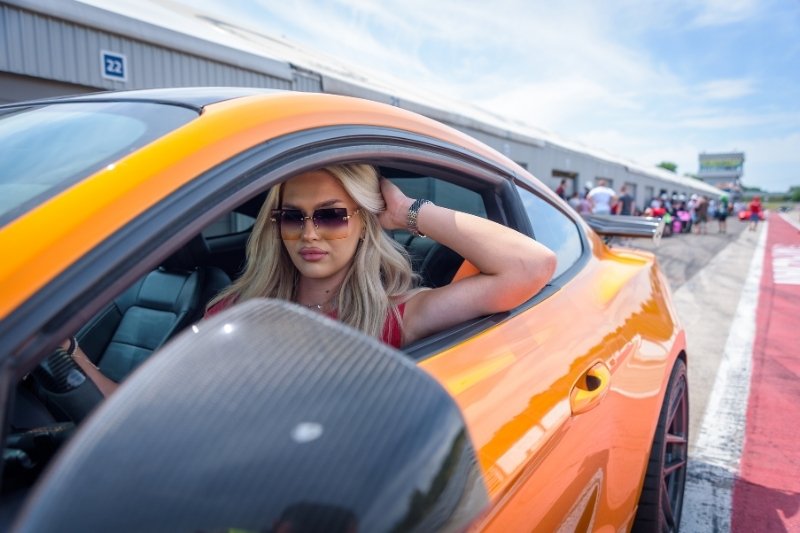 kobieta w pomarańczowym mustangu, na pierwszym tle karbonowe lusterko auta